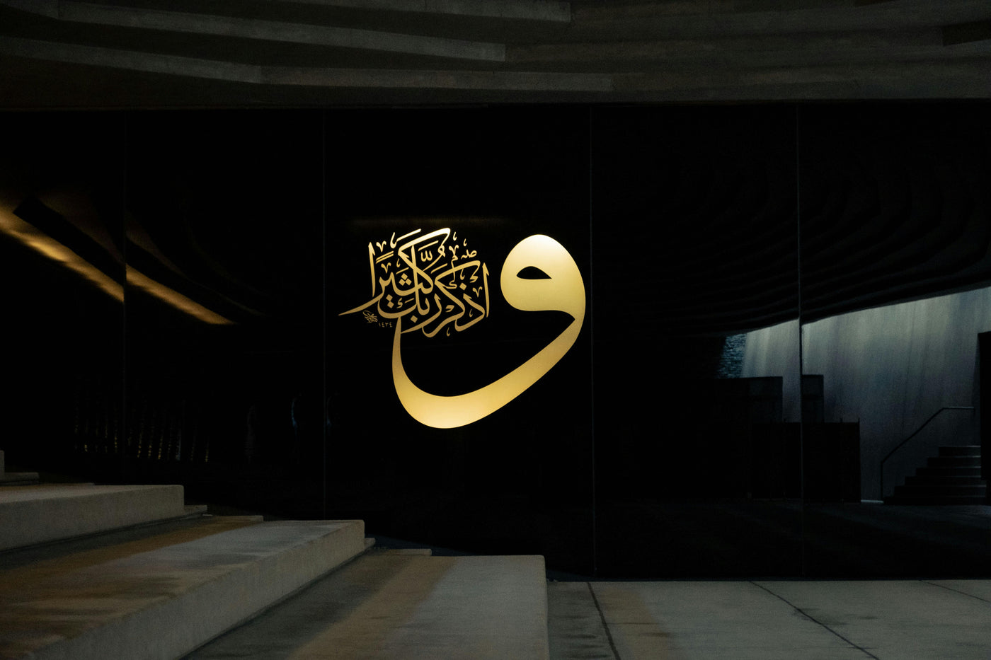 Golden Waw in Shadow - Large gold Arabic letter in a dark architectural space. Museum-grade framed artwork by Veriando Studio.